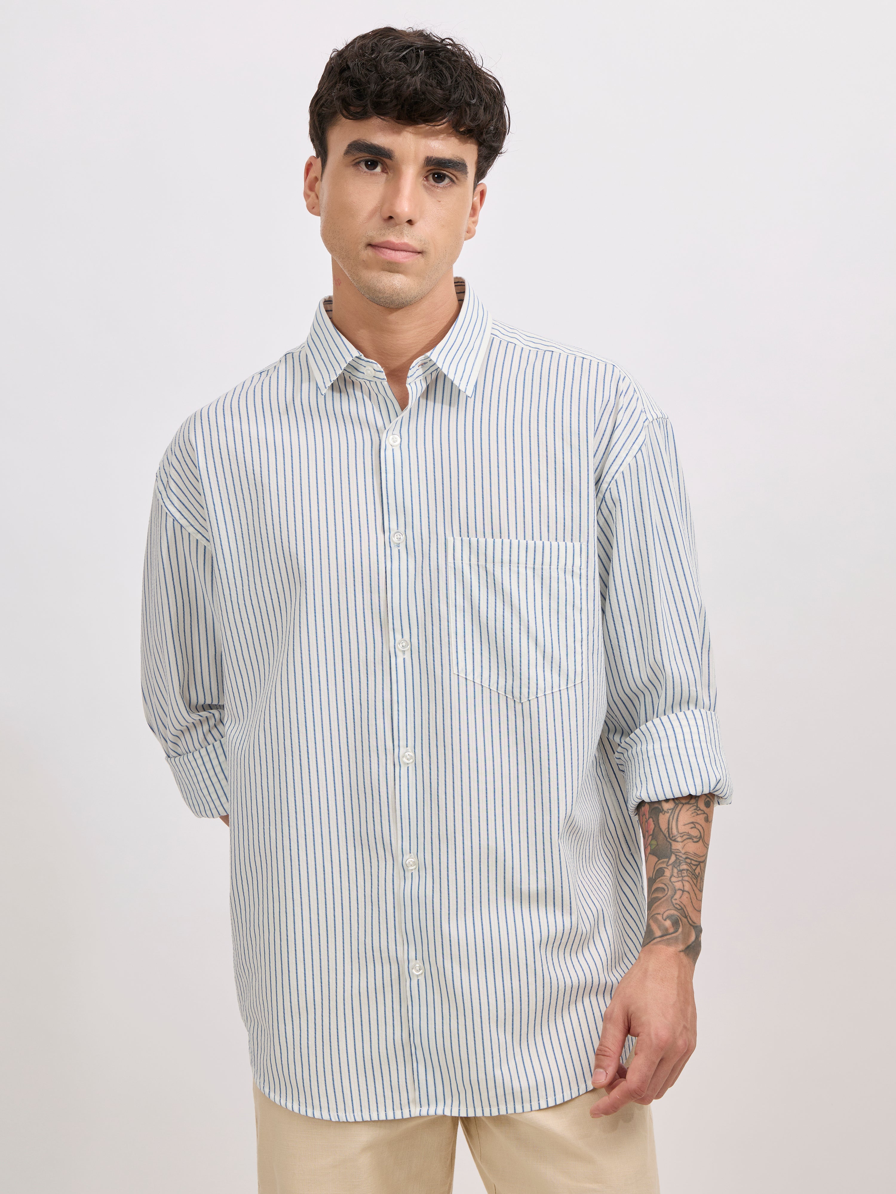 Man wearing a blue cotton oversized striped shirt with rolled sleeves, front pocket, and button-down collar
100% cotton
