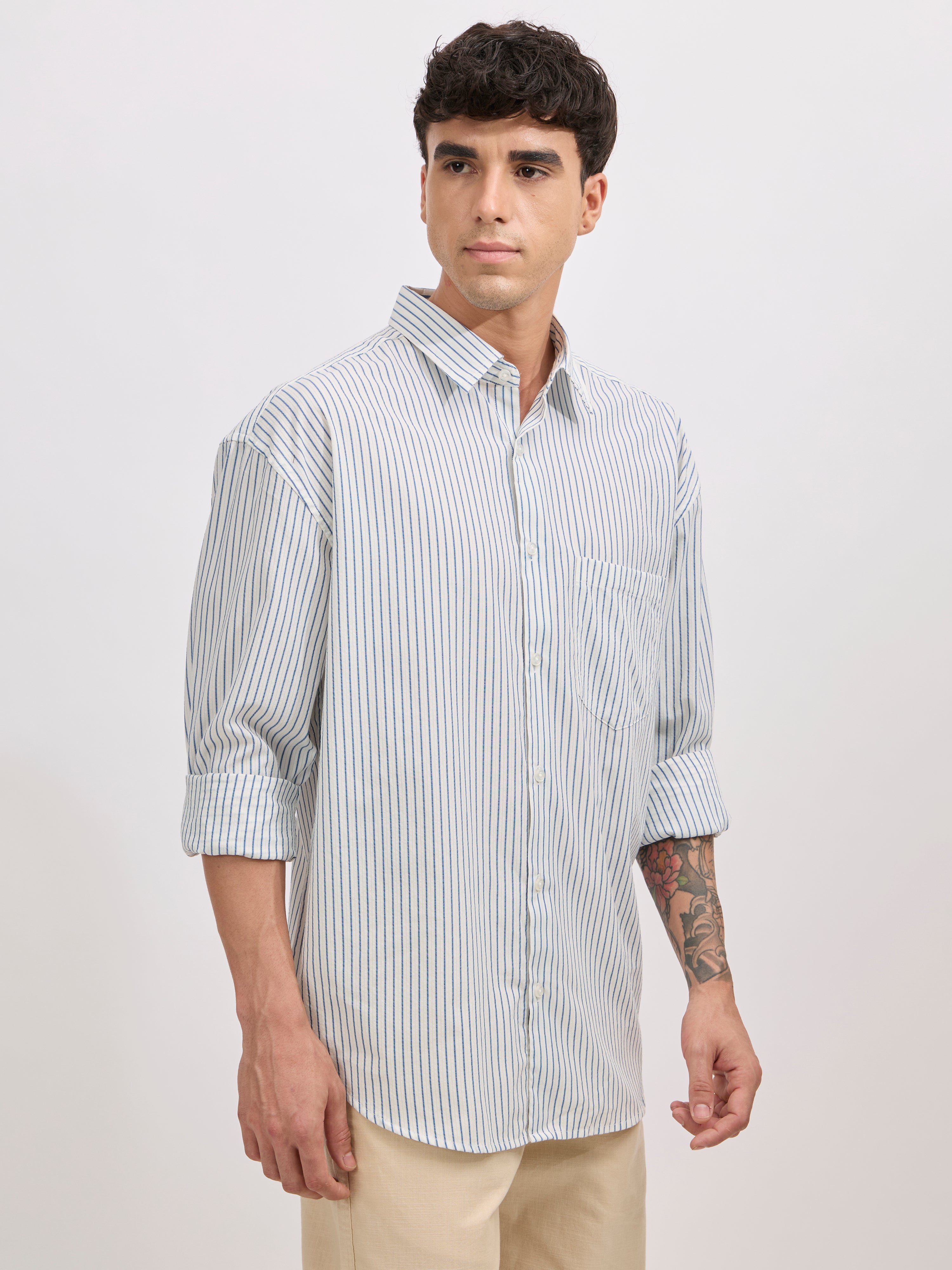 Man wearing a blue cotton oversized striped shirt with rolled sleeves, front pocket, and button-down collar
100% cotton
